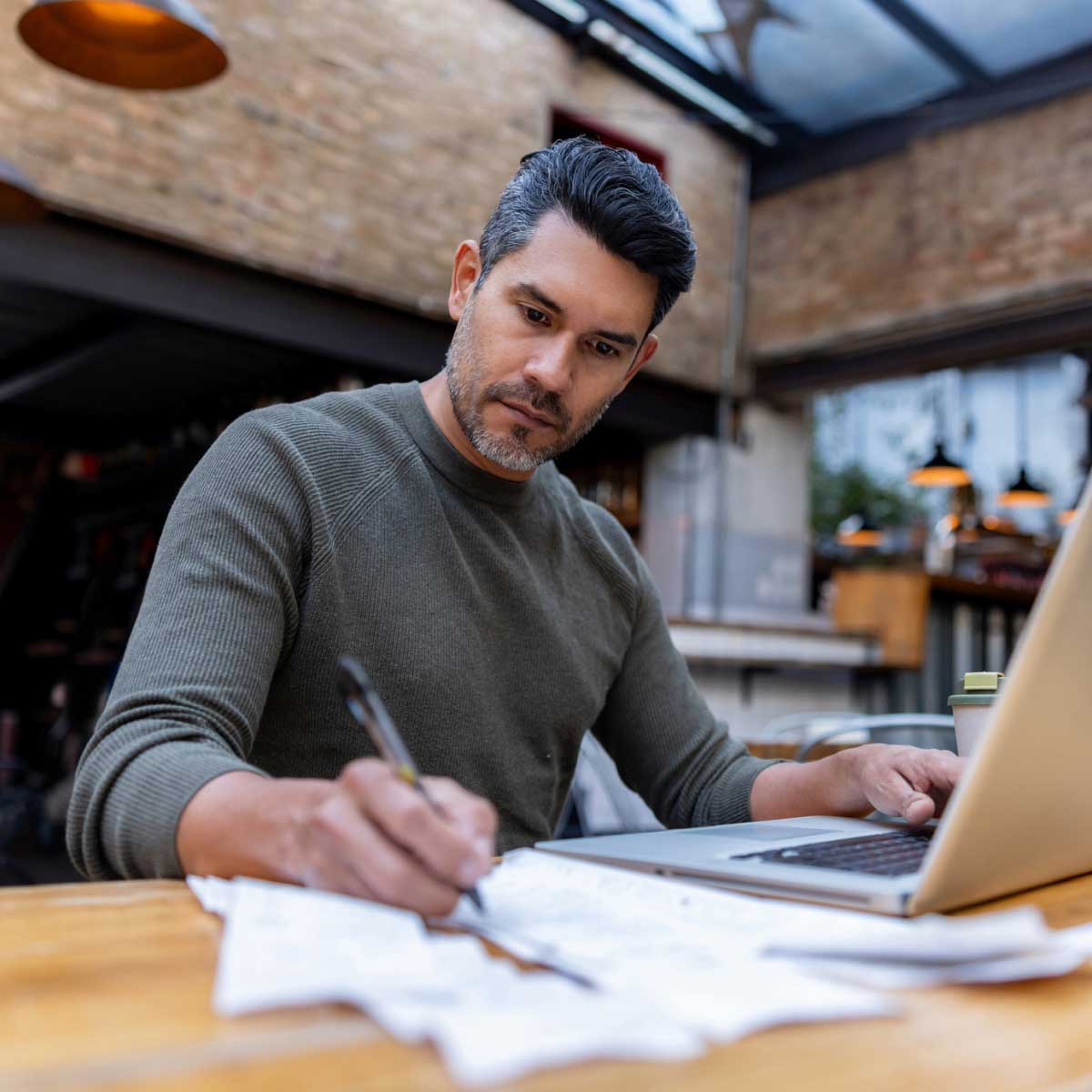 Business owner writing while doing finances on laptop