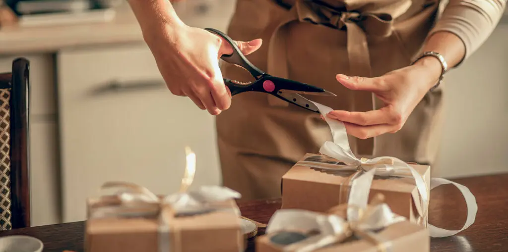 Person in apron cutting the ribbon on gift box