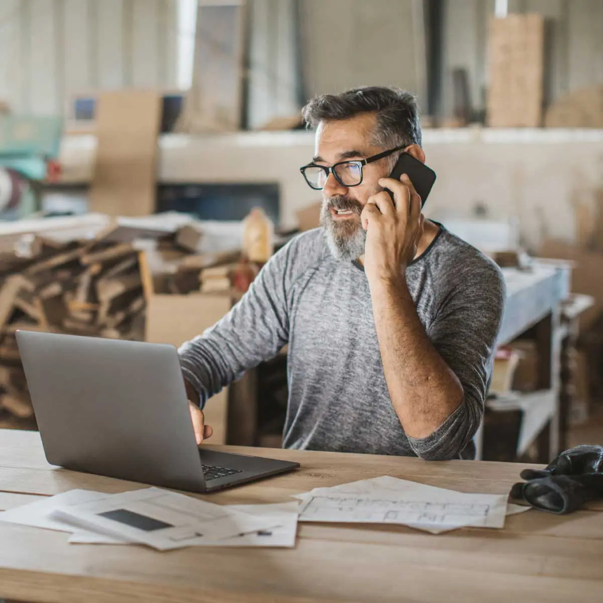 Carpenter on phone using laptop in workshop