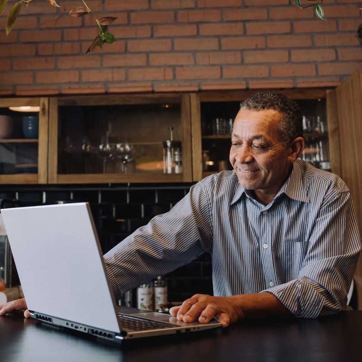 Person working on a laptop at a kitchen counter, with wooden cabinetry and a coffee machine behind them.